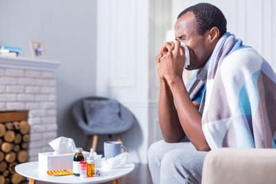 A man blows his nose while sitting on the couch