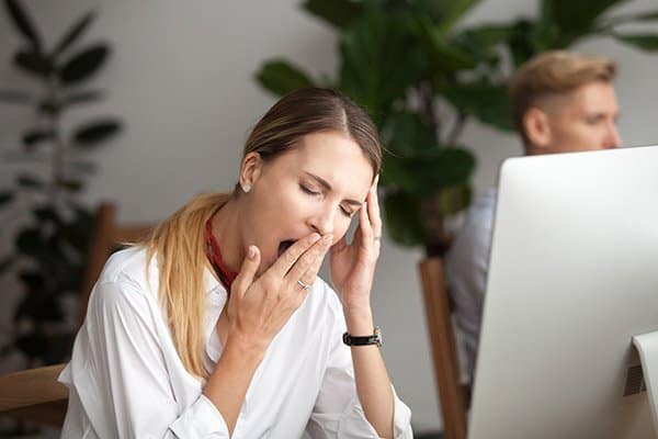 A tired woman yawns at her computer
