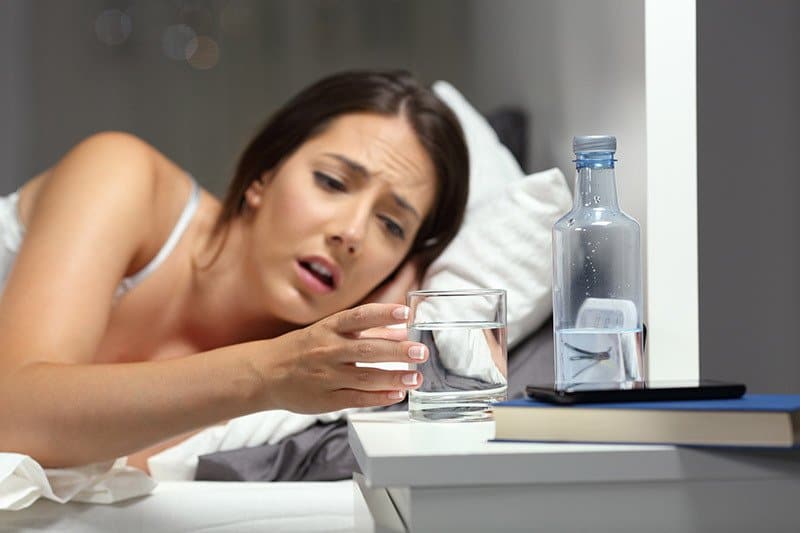 a woman drinks water in bed